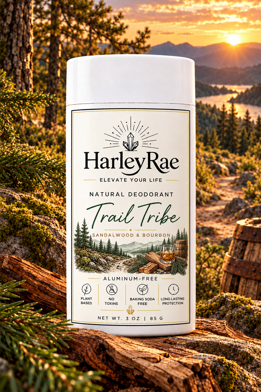 A 3 oz bottle of HarleyRae Trail Tribe natural deodorant stands on a log in a forest setting with a mountain sunset background. The bottle is white with a detailed label showing the brand name, scent description, and product features.