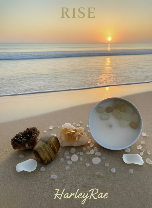 A white candle with clear liquid and citrine crystals on top, placed in a white bowl, with a wooden block and loose citrine crystals to the side, all set against a white fuzzy background.